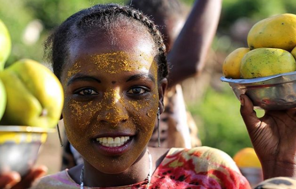 An Ethiopian girl from the town of Harar is smiling while holding bowls of mangoes. Her face is also covered in mangoes.