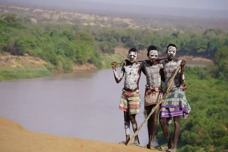 three young teenage boys dressed in traditional pain by a river in the omo valley